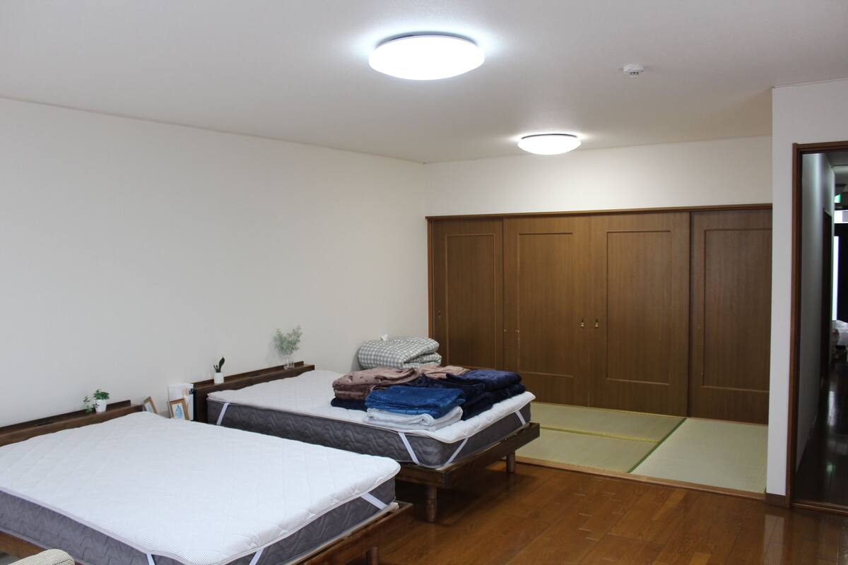 A room with two beds, a wooden wardrobe, and a futon.