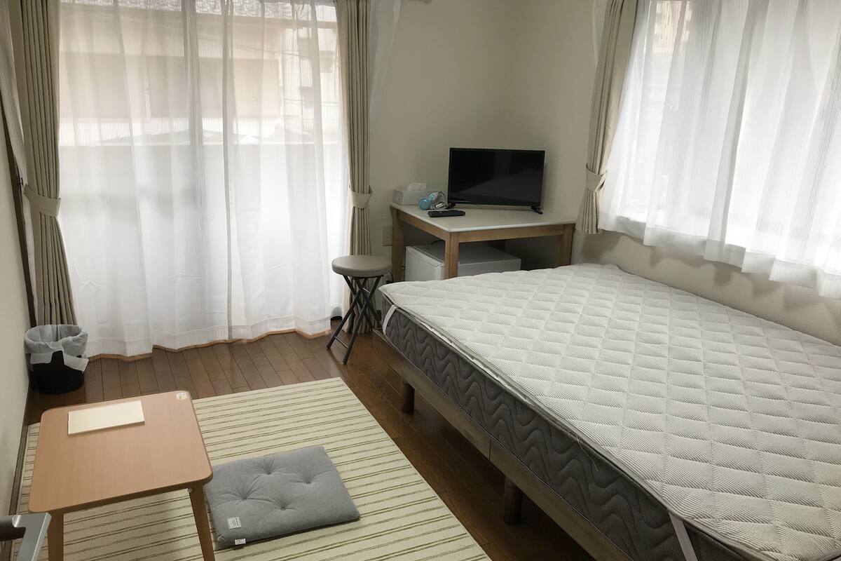 A bedroom with a bed, a desk, a chair, and a television.