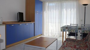Ett kompakt bostadsutrymme med ett litet kök, en matplats med ett mönstrat bordsduks och en soffa med en färgstark design.