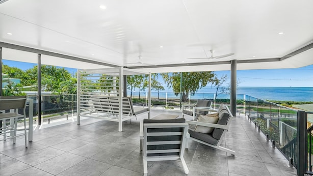 En rymlig balkong med utsikt över havet, inredd med moderna sittmöbler och en pergola.