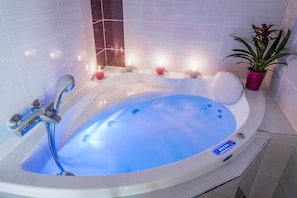Un baño moderno con una bañera grande, un cabezal de ducha de mano y una planta en maceta.