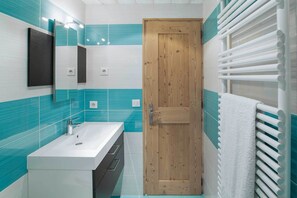 Un baño con puerta de madera, un lavamanos blanco y un perchero para toallas.