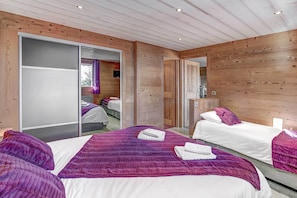 Two single beds with white linens and purple accents, a large mirror, and a radiator.