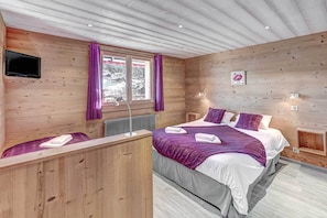 Una habitación con paneles de madera, una cama, un televisor y una ventana con cortinas moradas.