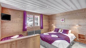 A wooden cabin bedroom with a bed, a desk, and a window with curtains.