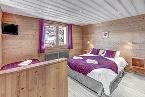 Un dormitorio de cabaña de madera con cama, escritorio y ventana con cortinas.