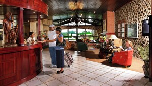 A lobby with a reception desk, a chandelier, a stone wall, and a red sofa. - Dog-friendly Farm Cottage in the Berg by First Private Stays (Drakensberg Gardens)