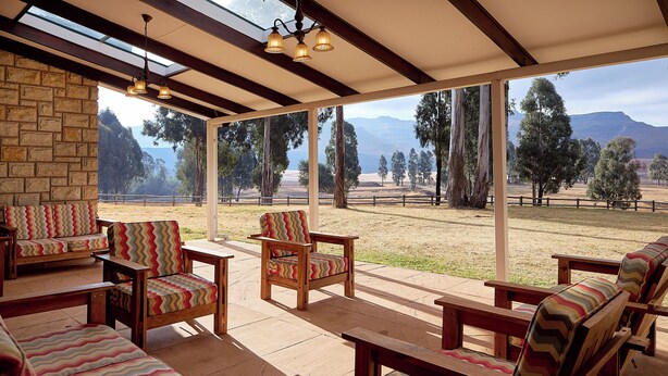 A covered outdoor seating area with wooden furniture and large windows offering a view of a grassy field and trees. - Dog-friendly Farm Cottage in the Berg by First Private Stays (Drakensberg Gardens)