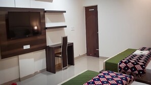 Un dormitorio con televisión montada en la pared, cama con ropa de cama estampada, un escritorio pequeño y una puerta.