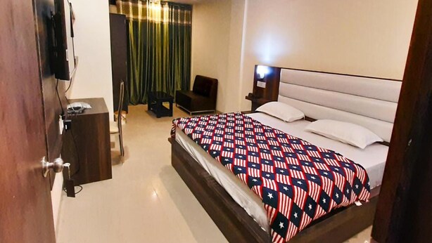 Habitación de hotel con cama, escritorio, silla, televisor y cortina.