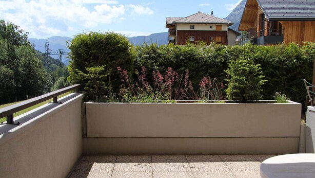 A terrace with a concrete floor, surrounded by greenery and a view of a mountain. - Cozy Apartment for 4-6 in Village Center with Terrace and Parking (BLA003) (Saint-Jean-de-Sixt)