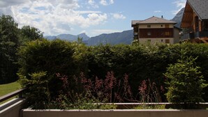 A building with a sloped roof, surrounded by lush greenery and mountains in the background. - Cozy Apartment for 4-6 in Village Center with Terrace and Parking (BLA003) (Saint-Jean-de-Sixt)