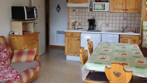 A compact kitchen with wooden cabinets, a microwave, a coffee maker, and a dining area with a table and chairs. - Cozy Apartment for 4-6 in Village Center with Terrace and Parking (BLA003) (Saint-Jean-de-Sixt)