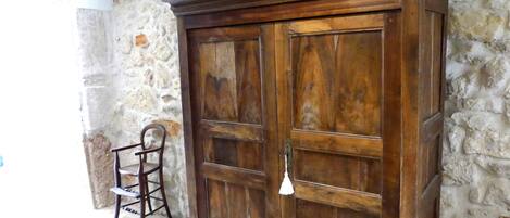 A wooden wardrobe with a large mirror and a chair in a stone-walled room.