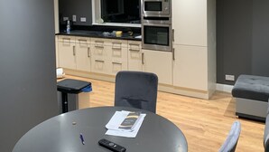 A modern kitchen with a microwave, oven, and dark countertops. There is a dining table with a remote control and papers on it. - Private Central Apartment Near Kilcullen (Calverstown)
