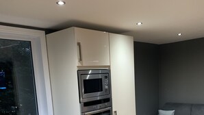 A modern kitchen with built-in appliances, a window, and a grey sofa in a living area. - Private Central Apartment Near Kilcullen (Calverstown)