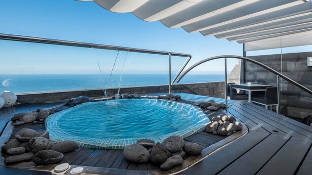 Un jacuzzi con vista al océano, rodeado de rocas y una terraza de madera.