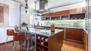 Una cocina moderna con una isla central, taburetes de bar y una mesa de comedor de vidrio.