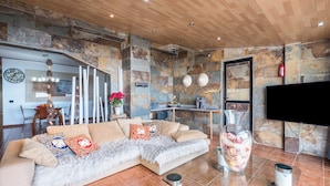 Un salón con sofá, televisor y pared de piedra.