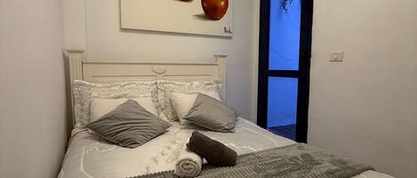 A bedroom with a bed, pillows, a blanket, and a wall-mounted painting of apples.
