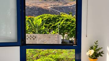 Una ventana con vista a un jardín ajardinado que incluye árboles y una cadena montañosa distante.