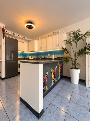 Una cocina moderna con armarios blancos, un refrigerador negro, una isla colorida y una planta en maceta.