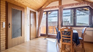 A wooden interior with a dining area, a window with curtains, and a door with a metal mesh.