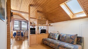 A cozy room with a wooden ceiling, a sofa, a dining area, and a skylight.