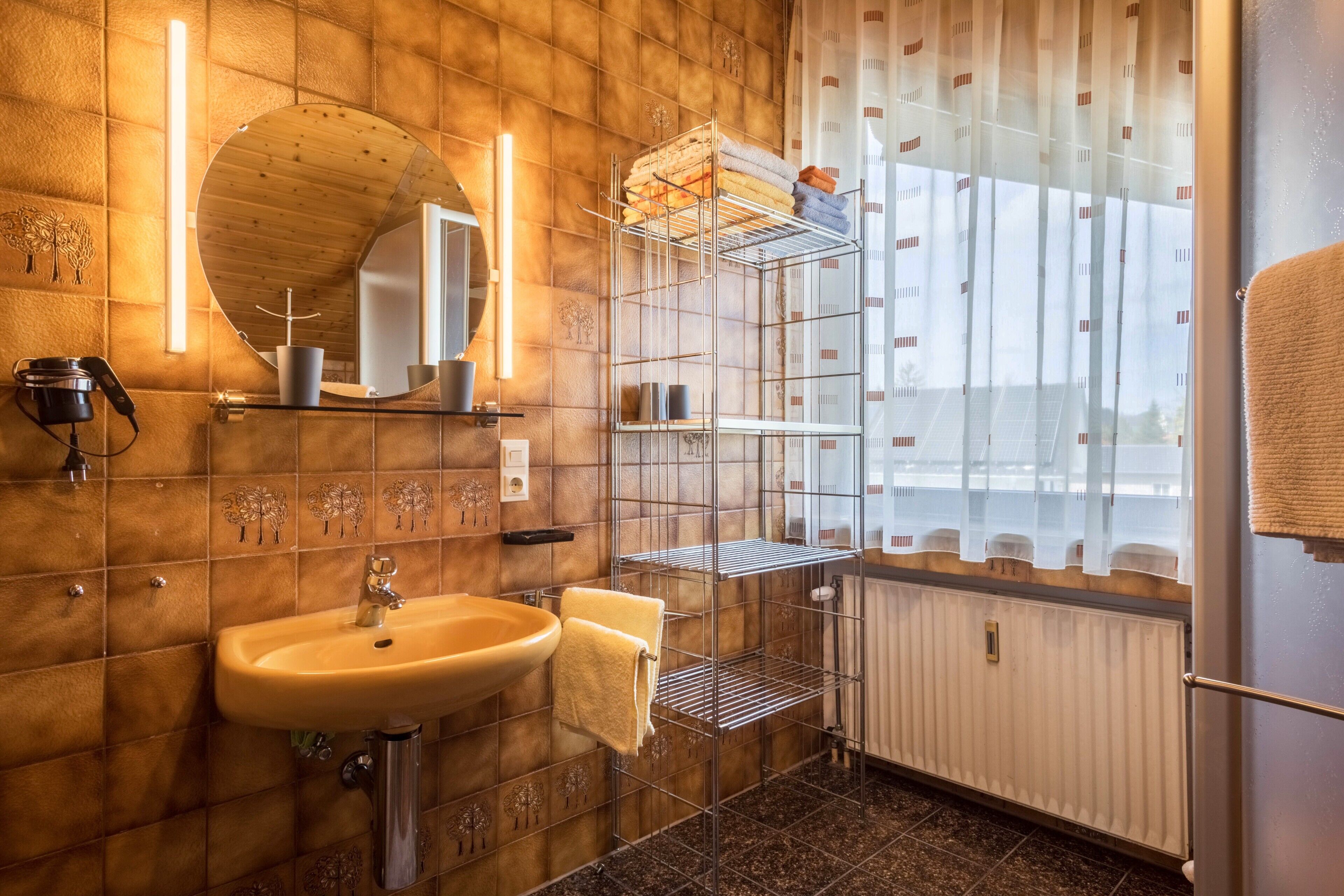 Een badkamer met een houten wand, een wastafel, een spiegel, een handdoekhouder en een raam met gordijnen.