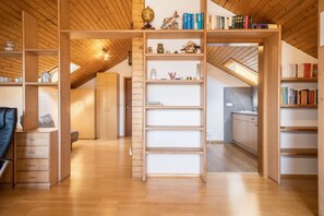 Een ruime loft met houten balken, een entresol met boekenkasten, en een keukenhoek.