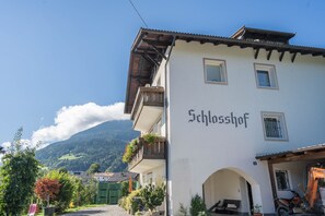 A building with 'Schlosshof' written on the side, a balcony with flowers, and a mountain in the background.