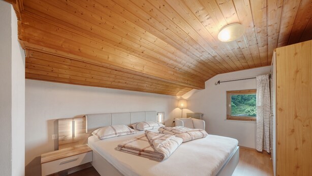 Une chambre avec un plafond en bois, un lit avec une literie blanche, des lampes de chevet et une fenêtre avec des rideaux.