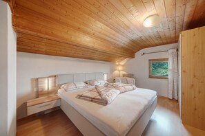 Ein Schlafzimmer mit Holzbalkendecke, einem Bett mit weißer Bettwäsche, Nachttischlampen und einem Fenster mit Vorhängen.