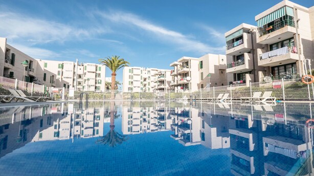 Una piscina amb aigua blava cristal·lina, envoltada d'edificis moderns amb balcons i una palmera.
