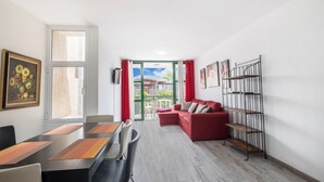 Un saló modern amb zona de menjador, sofà vermell i una prestatgeria metàl·lica.