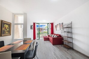 A modern living room with a dining area, red sofa, and a metal bookshelf.