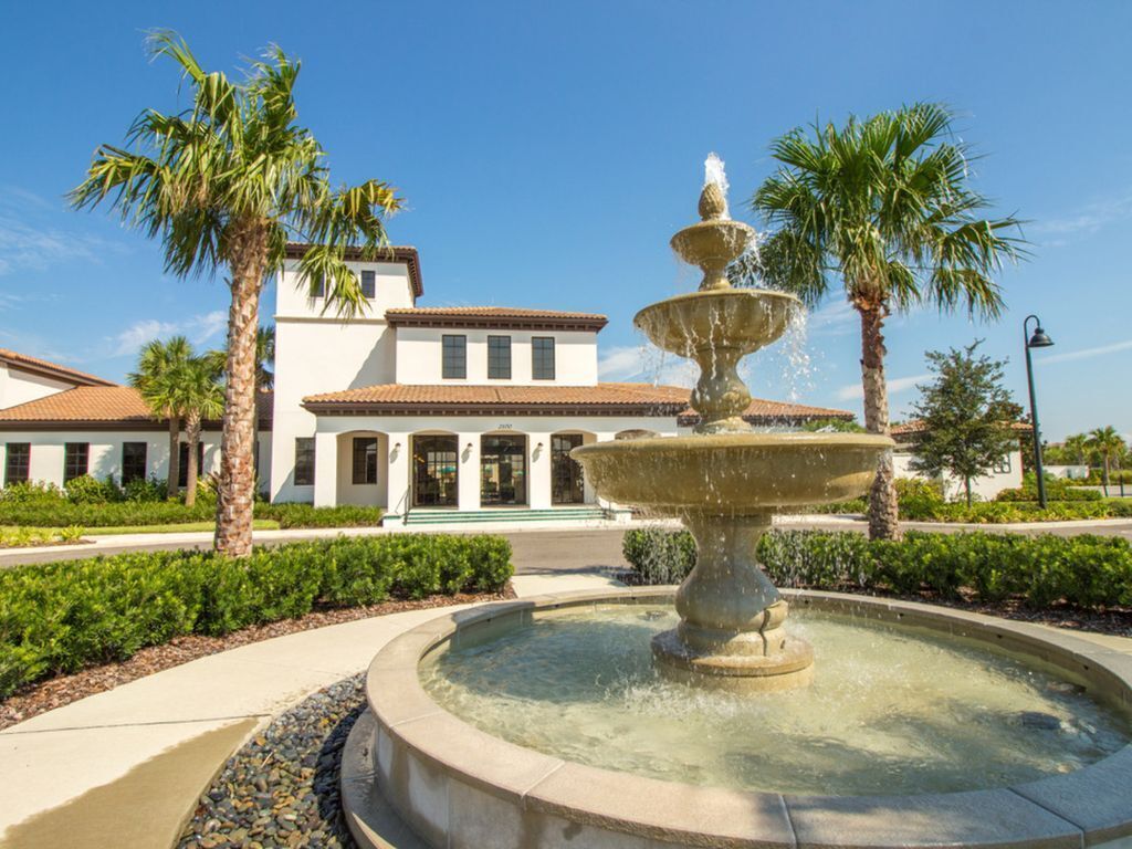A fountain with multiple tiers in a landscaped area with palm trees and a building in the background.