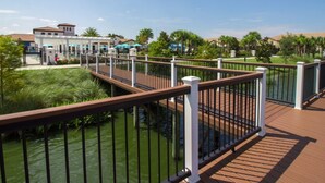 A wooden deck with a metal railing overlooking a body of water, surrounded by greenery and buildings.