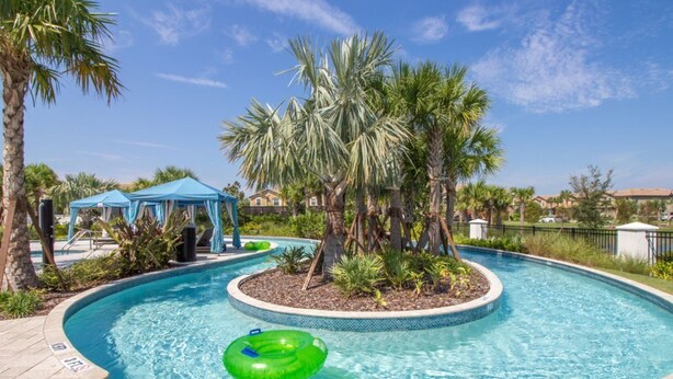 A swimming pool with a green inflatable ring, surrounded by palm trees and a blue gazebo.