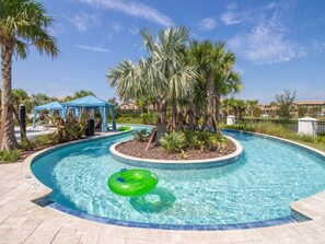 A swimming pool with a green inflatable ring, surrounded by palm trees and a blue gazebo. - 9BR | Large Pool Home | Clubhouse | Gated (Kissimmee)