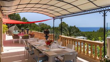 A covered outdoor dining area with tables and chairs, overlooking a scenic view of the sea.