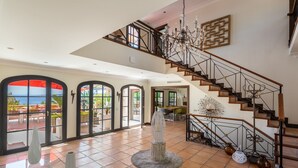 Un interior espacioso con una imponente escalera, ventanas amplias y una pieza decorativa central.
