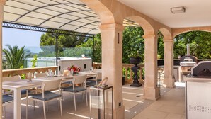 Un patio exterior con mesas y sillas, una parrilla y vistas del paisaje.
