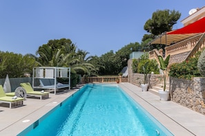 Una piscina con sillones de descanso, una pérgola y un muro de piedra con plantas en macetas.