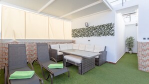 Un espace extérieur aménagé avec des meubles en osier, du gazon synthétique et un mur décoratif.