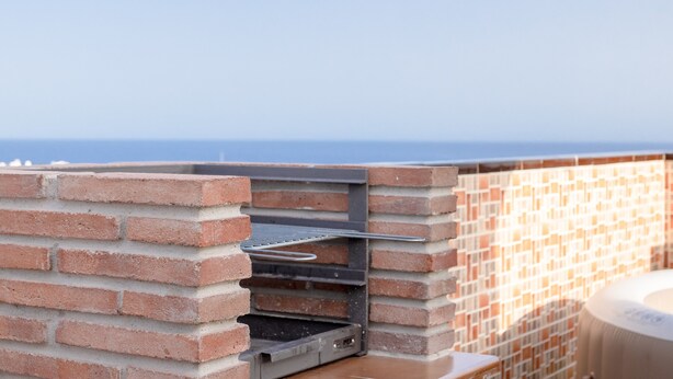 Un barbecue en briques installé à l’extérieur, doté d’une grille en métal, et offrant une vue sur une étendue d’eau.