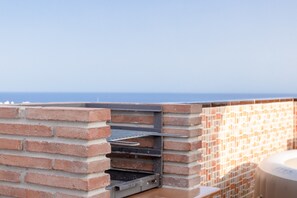 An outdoor brick barbecue grill with a metal rack, overlooking a body of water.