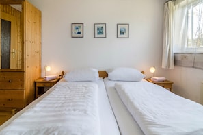 A double bed with white linens, two bedside tables with lamps, a wooden wardrobe, and three framed pictures on the wall.