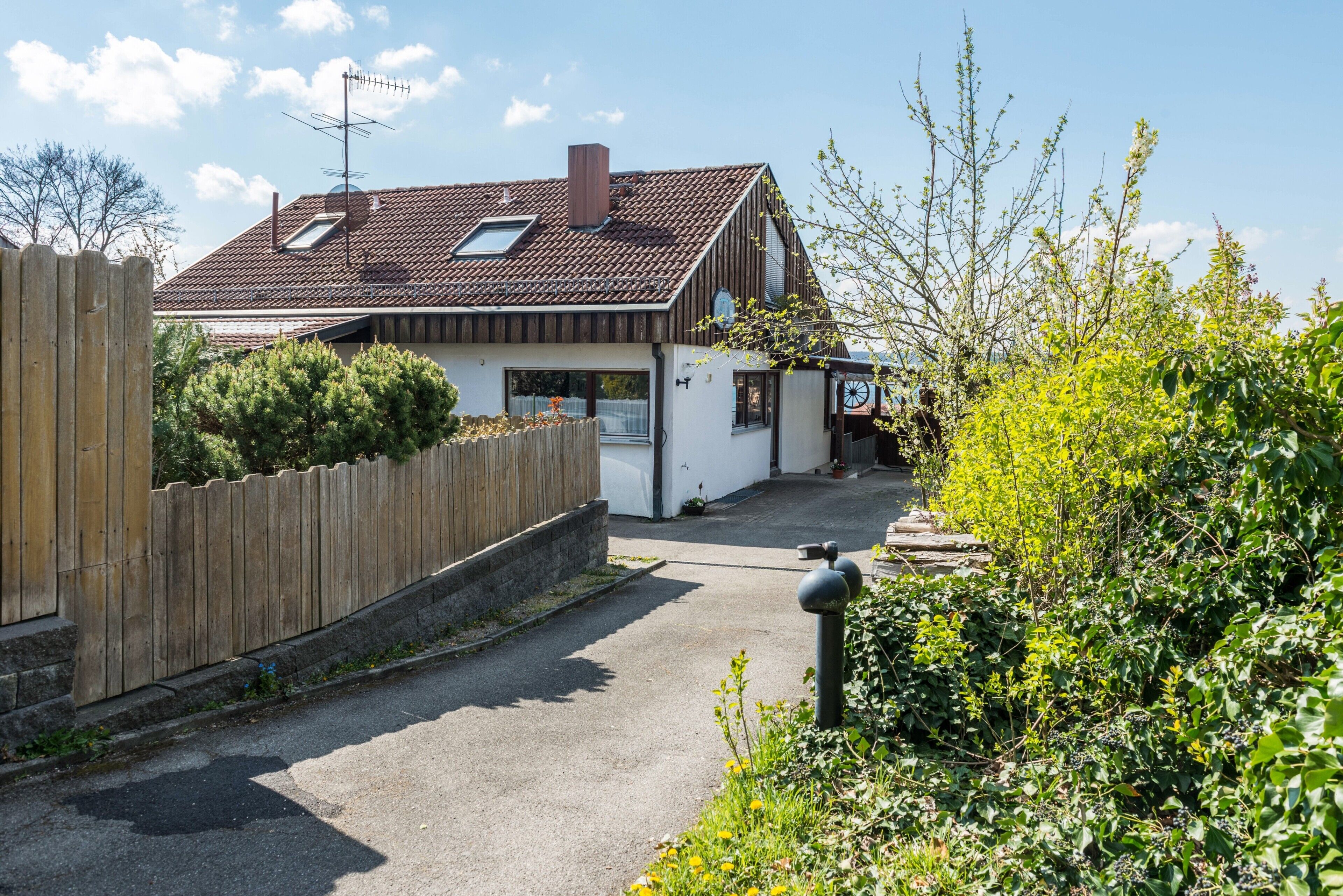 Ein Wohnhaus mit schrägem Dach, Holzlattenzaun und befestigter Auffahrt.