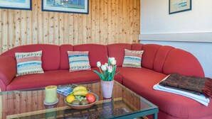 A red sofa with patterned cushions, a glass coffee table with fruit and a candle, and wooden paneling on the wall. - Holiday Apartment "Munding" with Garden, Terrace, Lake View, Grill & SAT-TV (Überlingen)